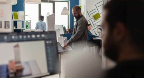 Engineer looking at blueprints on laptop at desk with architectural model of office buildings. Architect working with computer to create modern design concept of residential urban project.