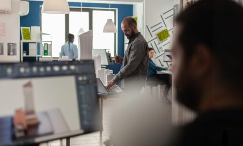 Engineer looking at blueprints on laptop at desk with architectural model of office buildings. Architect working with computer to create modern design concept of residential urban project.