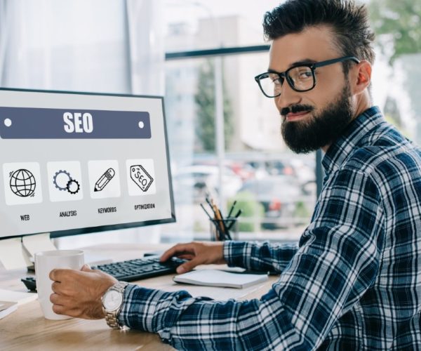 young successful seo manager sitting at workplace with computer and looking at camera